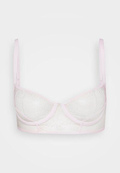 Kerge roosa rinnahoidja, millel on läbipaistvad, tikitud karbid ja reguleeritavad rihmad valgelt taustalt.