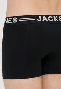 Mustat boxeri alusvaatteet, joissa on leveä joustava vyötärö ja valkoinen logo. Kangas näyttää pehmeältä ja sileältä.