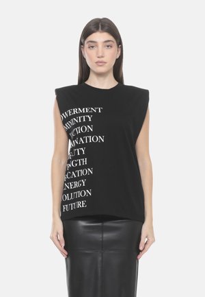 Donna con capelli castani lisci, indossa un top nero senza maniche con parole ispiratrici bianche e una gonna di pelle nera, rivolta in avanti.