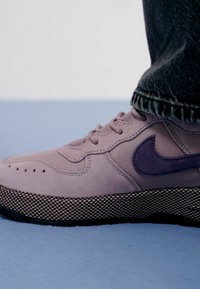 Zapatilla de cuero rosa con un swoosh texturizado púrpura, punta redondeada, perforaciones para ventilación y una suela de malla negra.