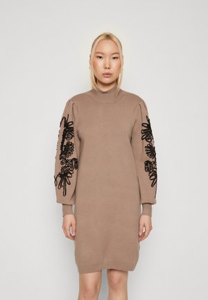 Strikket kjole i beige med høj hals, med sort blomstermotiver på puffede ærmer og ribbede manchetter. Blød tekstur, knælangt design.
