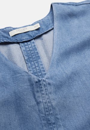 Hellblaues Jeanshemd mit V-Ausschnitt und sichtbaren vertikalen Nähten entlang des Halsausschnitts sowie einem Kragenetikett mit der Aufschrift "Cellbes".