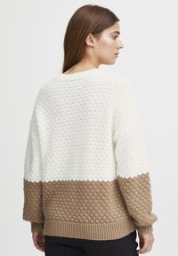 Strickpullover mit strukturiertem Design, wobei der obere Teil in Creme und der untere Teil in Braun gehalten ist. Rippbündchen und Saum sorgen für zusätzliche Definition.