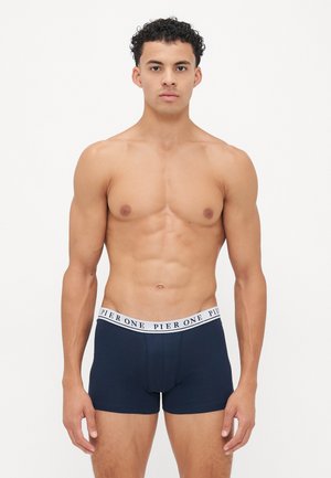 Boxer-briefs bleu marine avec une ceinture élastique blanche marquée "PIER ONE." Le tissu semble lisse et extensible, épousant étroitement le corps.