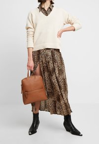 Pull crème texturé avec un décolleté en V profond, associé à une jupe imprimée léopard, des bottines noires à talons pointus et un sac à dos en cuir marron.