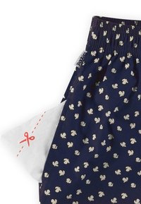 Marineblauwe stof met witte bloemmotieven, voorzien van een elastische tailleband. Een klein wit zakje met een rode schaarafbeelding is gedeeltelijk zichtbaar.