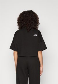 Svart kort topp med en texturerad design. Har korta ärmar och en liten vit logotyp på övre delen av ryggen. Matchas med byxor i samma stil.