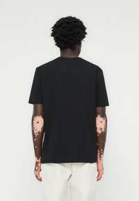 Zwart T-shirt met korte mouwen gemaakt van katoen, met een ronde hals, een relaxte pasvorm en een gladde textuur, gedragen met lichtgekleurde broek.
