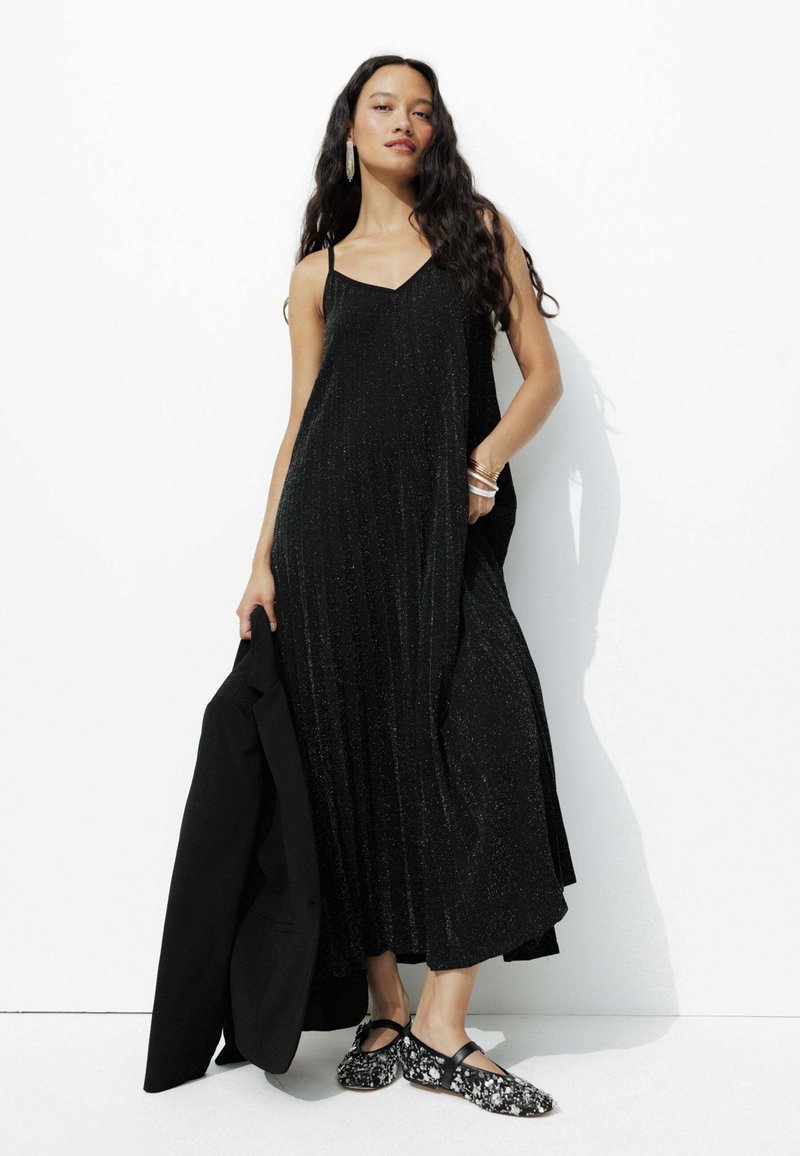 Robe maxi plissée noire avec des bretelles fines et un subtil éclat, assortie à un blazer noir et des ballerines à motif. Tissu lisse avec une silhouette fluide.