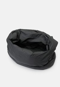 Saco de tecido preto, macio, com uma superfície texturizada, de forma oval e um bolso interior com fecho. Design leve e flexível.