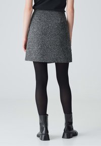 Grijze tweed A-lijn rok met een gestructureerd oppervlak, voorzien van twee zijzakken en een subtiel patroon. Draagt met zwarte panty en enkellaarsjes.