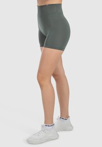 Bermudas de talle alto en color verde, confeccionadas con un material elástico. Presentan una textura suave y una costura detallada. Se combinan con zapatillas deportivas blancas.