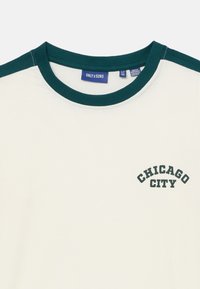 Vitt t-shirt med mörkgröna detaljer på axlarna, med en böjd text "CHICAGO CITY" i mörkgrönt framtill. Tillverkat av bomull.