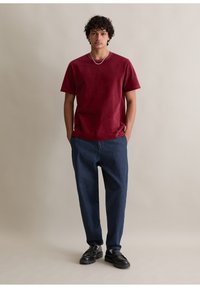 Bordowy t-shirt z krótkimi rękawami z miękkiego materiału, w połączeniu z luźnymi, ciemnoniebieskimi dżinsami. Czarne skórzane buty uzupełniają strój.