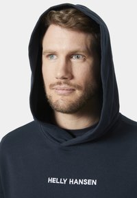 Marineblauwe hoodie van zacht materiaal, met een grote capuchon en het geborduurde "HELLY HANSEN" logo in het wit op de borst.