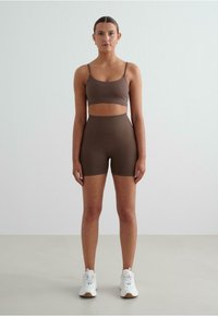 Bruin geribbelde sportbeha en shortset, met verstelbare bandjes en een hoge tailleband, gecombineerd met witte sportieve schoenen.