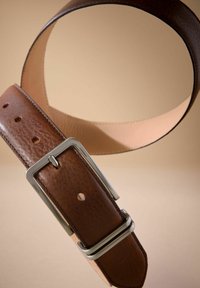 Cintura in pelle marrone con una texture liscia, fibbia rettangolare argentata e numerosi fori di regolazione. Il lato interno è di un beige più chiaro.