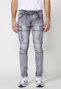 Grijze versleten cargo jeans met meerdere zijzakken, strakke pasvorm en contrasterende stiksels. Gepaard met witte sneakers.