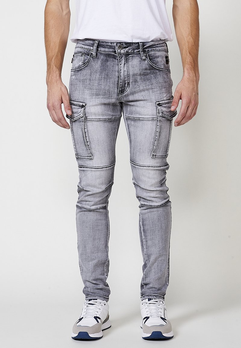 Grijze versleten cargo jeans met meerdere zijzakken, strakke pasvorm en contrasterende stiksels. Gepaard met witte sneakers.