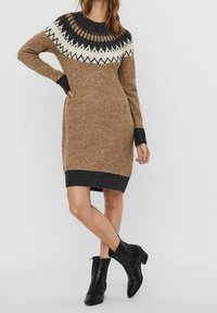 Robe pull en beige clair avec un empiècement à motif en noir et blanc. Les manches longues et les poignets et l'ourlet côtelés ajoutent de la texture.