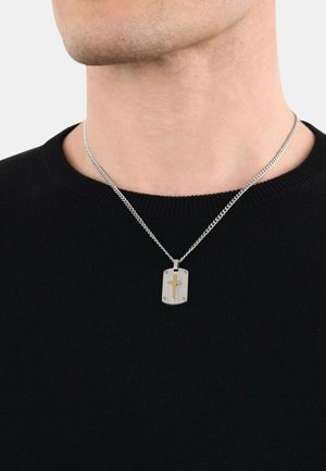 Silberner Anhänger mit einem goldenen Kreuzdesign, das strukturierte Akzente aufweist, an einer silbernen Kette befestigt und über einem schwarzen Pullover getragen.
