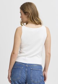 Weißes, ärmelloses Oberteil mit rundem Ausschnitt, kombiniert mit Jeans. Der Stoff wirkt weich mit einer glatten Textur und tailliertem Design.