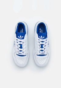 Zapatillas blancas Adidas con lengua e interior azul, cordones blancos y área perforada en la punta, vistas desde arriba sobre un fondo blanco.