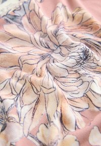 Textile floral en rose doux, présentant une texture lisse avec des contours détaillés de fleurs beige clair, créant un effet superposé et dimensionnel.