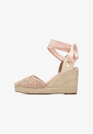 Alpargata de cuña en rosa claro, con parte superior de tela bordada, lazo de cinta en el tobillo, plataforma de yute trenzado y detalles texturizados en los lados.