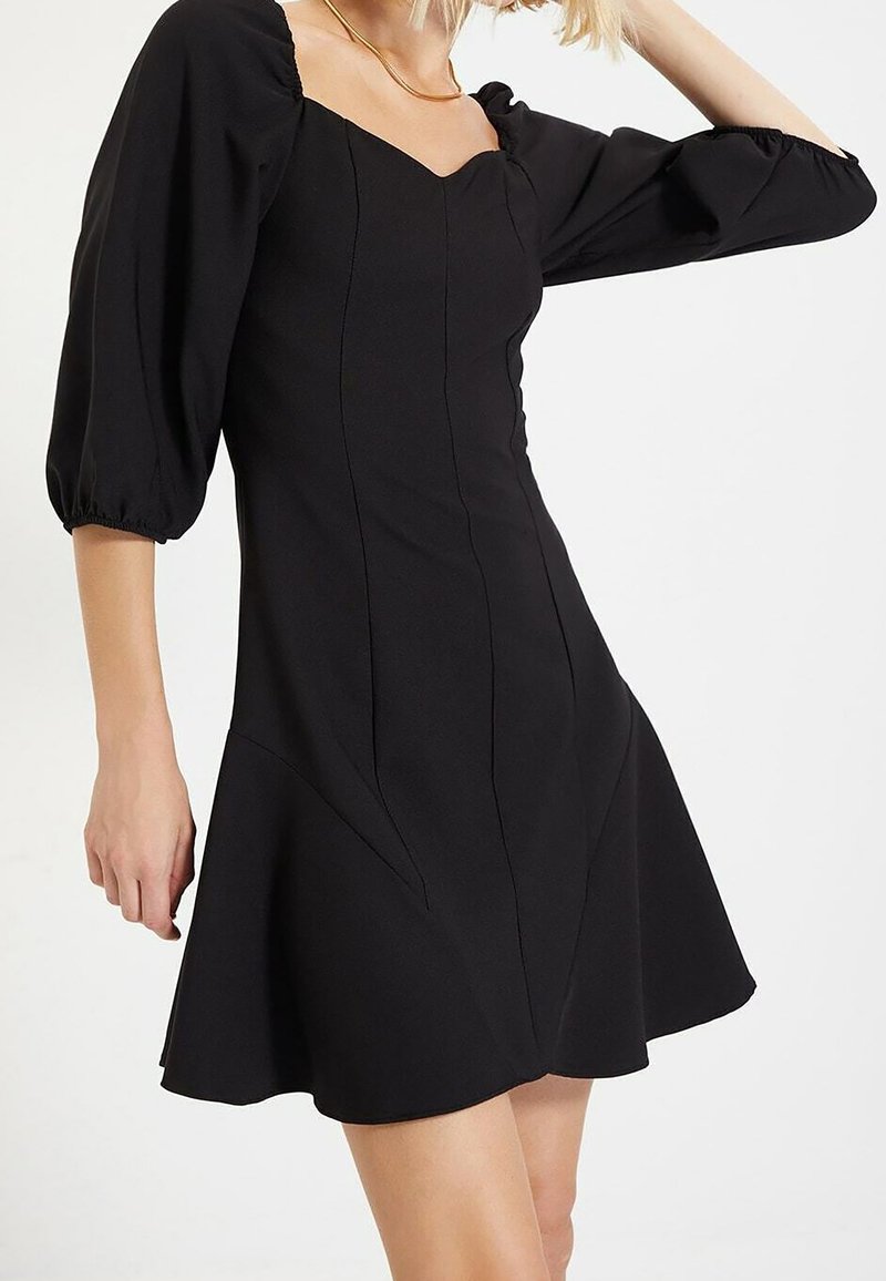 Vestido negro ajustado con mangas abullonadas, escote cuadrado y dobladillo acampanado, con costuras estructuradas para añadir forma y textura.