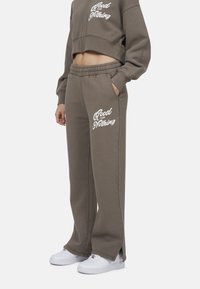 Felpa grigia a maniche lunghe con testo bianco, abbinata a pantaloni grigi con taglio laterale e dettagli sulle tasche, indossata con scarpe da ginnastica bianche.