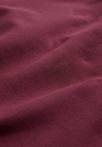 Close-up of smooth, maroon-colored fabric with fine knit texture and soft folds creating subtle shadows.