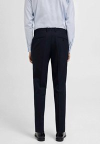 Dunkle, taillierte Hose mit geradem Schnitt, ausgestattet mit Gürtelschlaufen und zwei Gesäßtaschen, kombiniert mit einem hellblauen Hemd.
