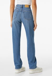 Jeans de tiro alto azul con corte recto, que cuentan con dos bolsillos en la parte trasera y un parche de cuero marrón en la cintura. Tela de mezclilla texturizada.