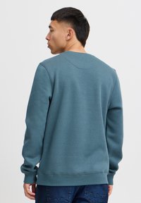 Felpa in verde teal tenue, realizzata in tessuto morbido. Presenta maniche lunghe, collo a giro e polsini a costine. Design semplice senza loghi visibili.