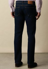 Jeans in denim blu scuro con un taglio classico a gamba dritta, dotati di tasche posteriori e un'etichetta in pelle marrone sulla vita.