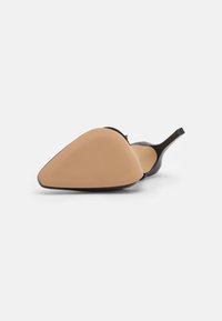 Černá lodička na vysokém podpatku s špičatou špičkou, hladkým svrškem a kontrastními tanovými gumovými podrážkami s horizontálním vroubkováním pro větší přilnavost.