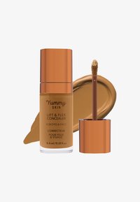 Lift & Flex Concealer fra Yummy Skin i en glassflaske med en bronsefargehette, utstyrt med en doe-foot applikator og en rik karamellkremfarge.