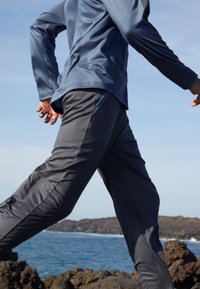 Atletische outfit met een blauwe top met lange mouwen en grijze broek met een slanke pasvorm, gemaakt van een soepele, lichte stof.