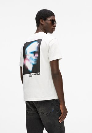 Camiseta blanca de algodón con un estampado gráfico en la parte trasera, que muestra un rostro distorsionado en tonos de azul y rosa, con texto negro debajo.