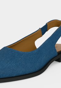 Μπλε υφασμάτινο παπούτσι με λουράκι στο πίσω μέρος, μαύρη σόλα και κάμελα εσωτερική επένδυση, κοντινή λήψη από το πλάι και με ανοιχτό λουράκι στη φτέρνα.