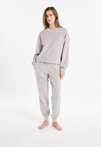 Set di abbigliamento comodo grigio chiaro a coste, composto da una felpa girocollo e pantaloni affusolati, che mostra una texture morbida e una vestibilità rilassata.