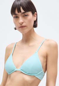 Top de bikini albastru deschis, cu model în dungi, design triunghiular, bretele subțiri și cusătură centrală. Materialul are o textură netedă și moale.