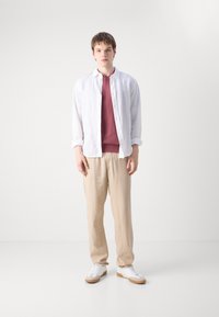 Hvit lin skjorte med knapper over en bordeaux genser, parret med beige linbukser og hvite joggesko med lys brun såle. Enkle og nøytrale toner.