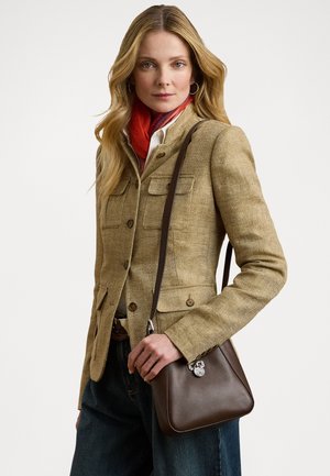 Blazer cu model herringbone de culoare bej, cu două buzunare frontale, purtat peste o cămașă albă și o eșarfă roșie; ținând o geantă mică de umăr de culoare maro. Blugi închiși la culoare.