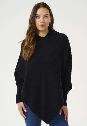 Black knitted poncho with textured herringbone pattern, featuring a draped design and diagonal hem. Long sleeves extend from shoulders.