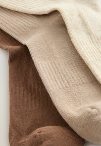 Drie paar geribde sokken in verschillende tinten: donkerbruin, beige en lichtroom. Ze hebben een zachte textuur en een consistente breipatroon.