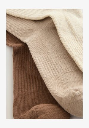 Három pár bordázott zokni különböző árnyalatokban: sötétbarna, bézs és világoskrém. Puha textúrával és egységes kötésmintával rendelkeznek.