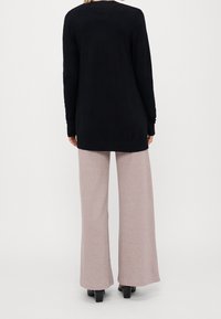 Suéter negro de manga larga con detalle acanalado, combinado con pantalones de pierna ancha rosa claro en una tela suave y texturizada. Zapatos de tacón negros visibles.