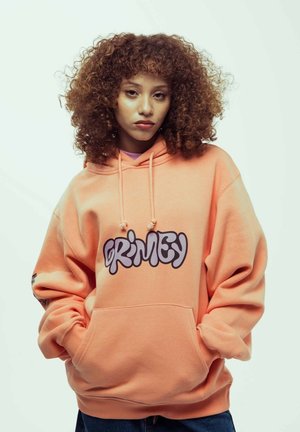 Sudadera oversized de color melocotón con un gran logo gris "GRIMEY" en la parte delantera, un bolsillo canguro y capucha ajustable con cordón.